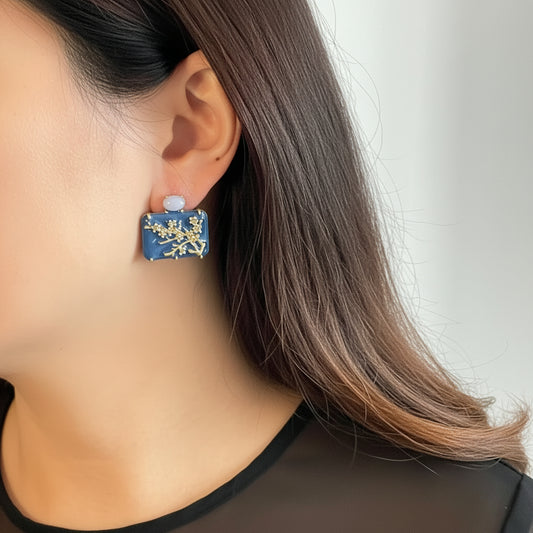 Close-up of a person wearing a blue floral earring with a plain background