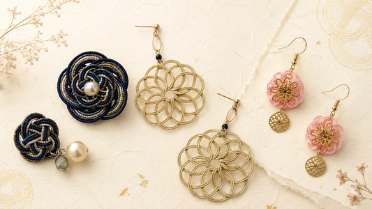 Elegant Mizuhiki jewellery arranged on textured ivory paper, featuring navy pearl knotwork, gold floral earrings, and pink Japanese-inspired drop earrings.