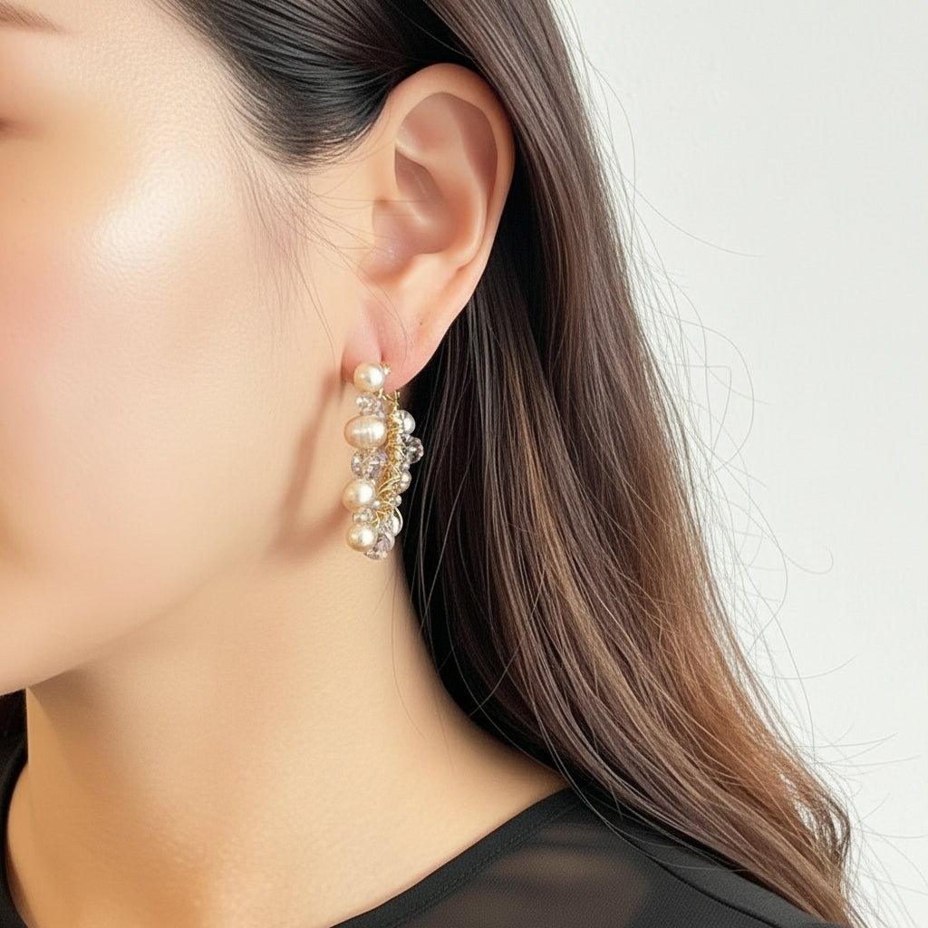 Close-up of an ear wearing gold hoop earrings with pearls and crystals on a neutral background.