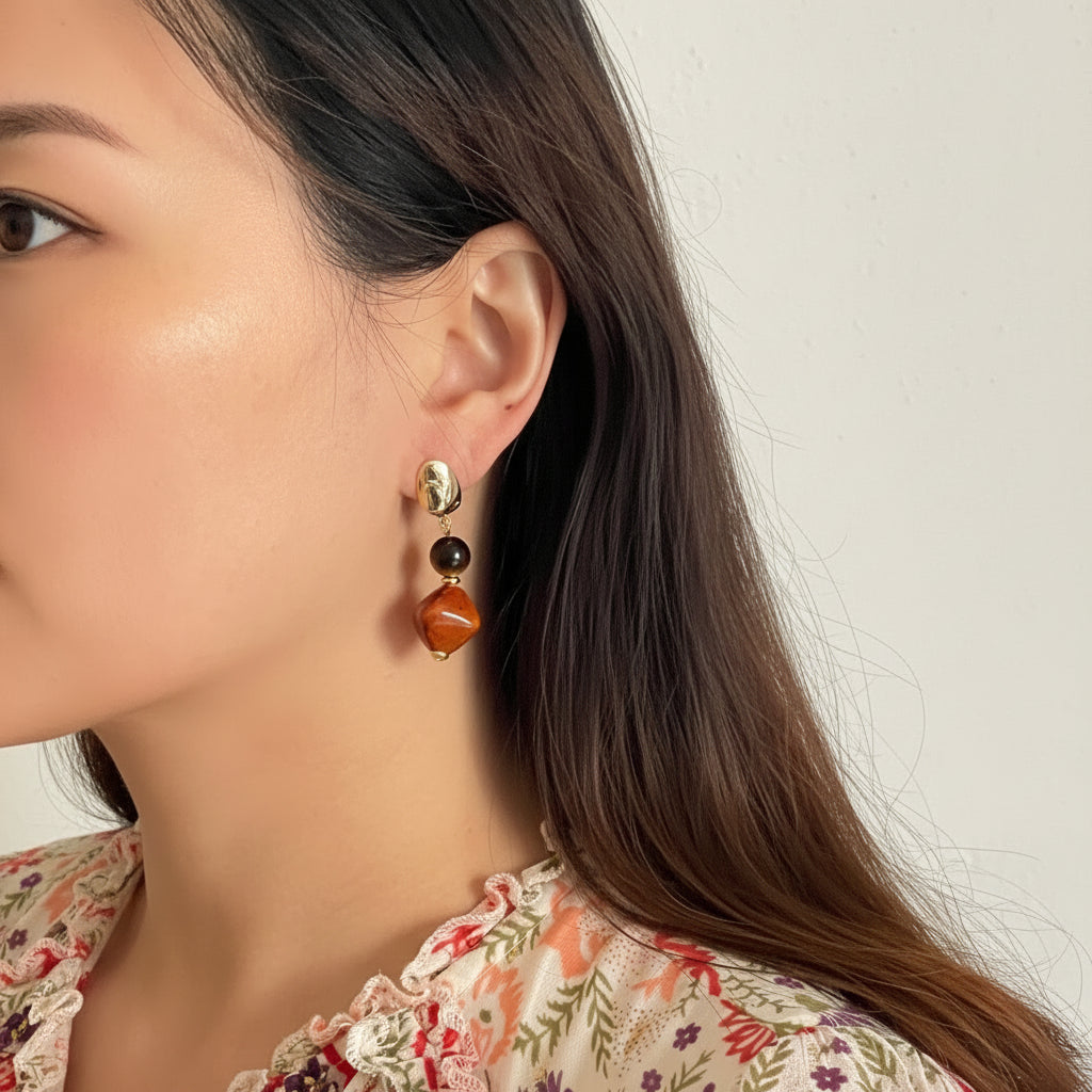 Close-up of a person wearing a gold, black, and brown beaded earring against a neutral background.