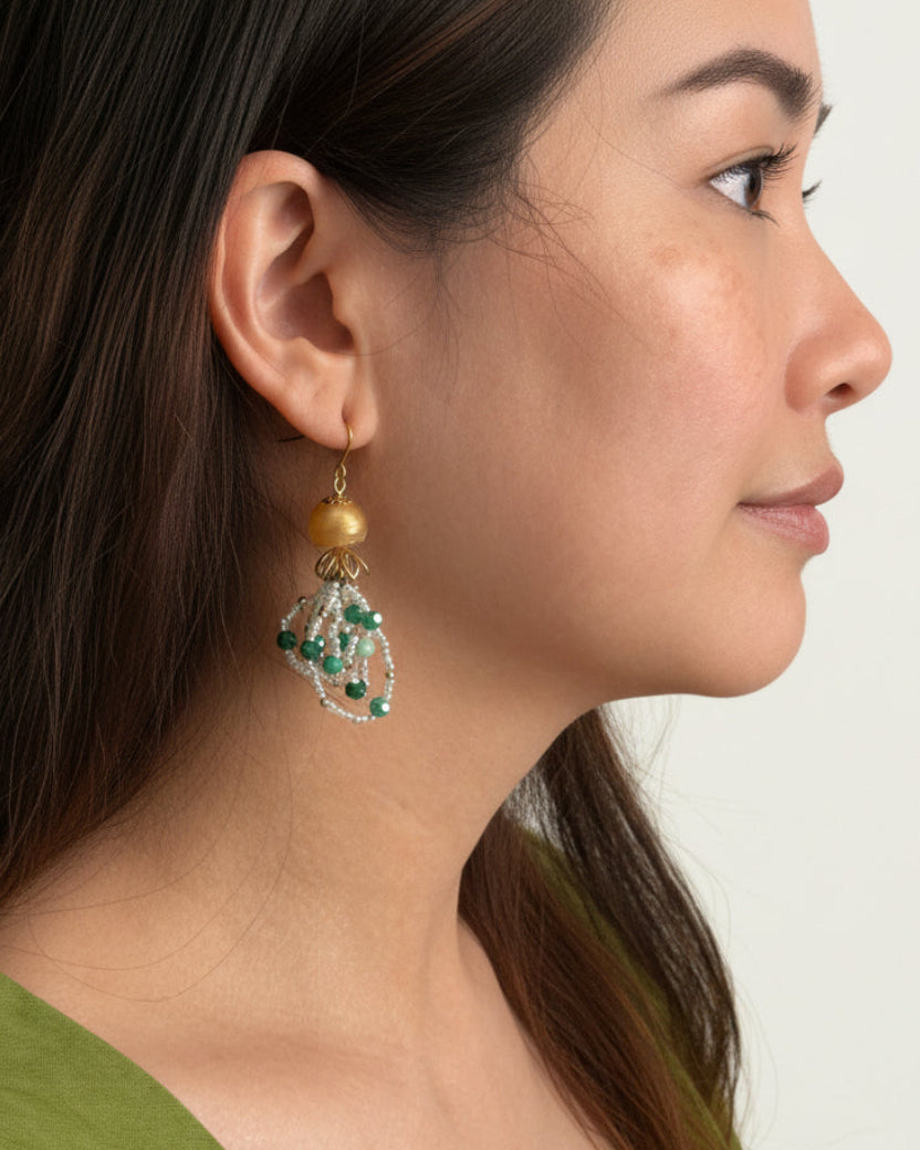 Woman wearing a gold earring with green gemstones on a white background