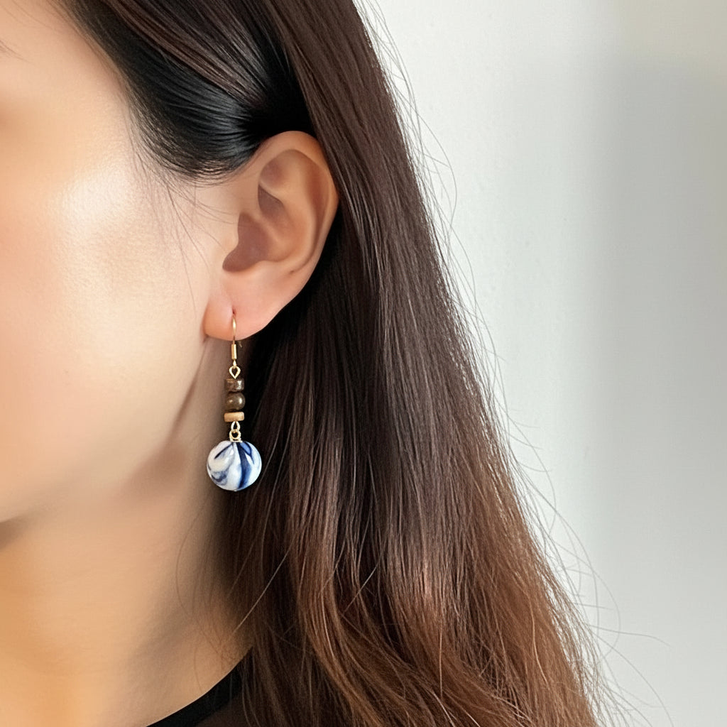 Close-up of an ear wearing a indigo tie dye fabric earring with a plain background