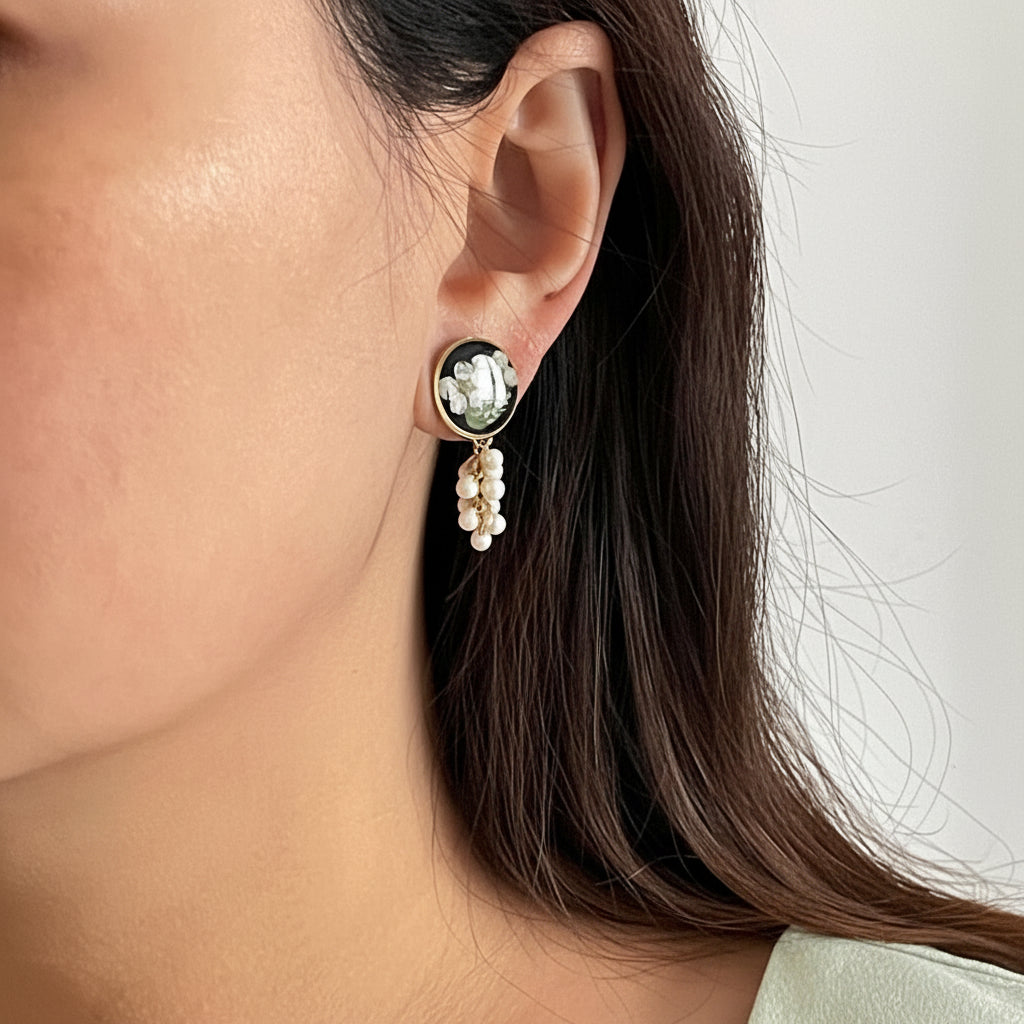 Close-up of an ear wearing a decorative earring with a pearl drop on a neutral background
