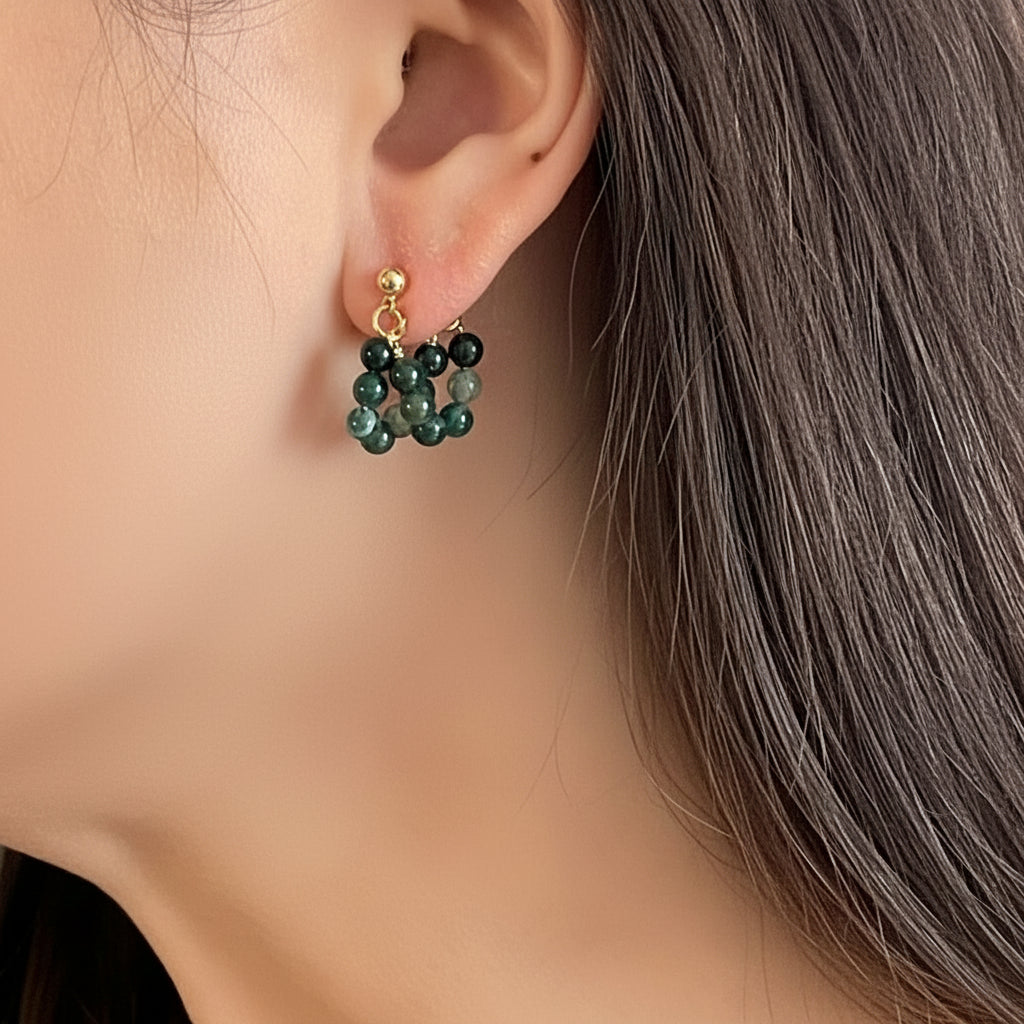 Close-up of an ear wearing a green beaded earring with gold accents.