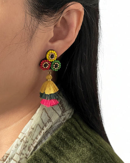 Close-up of a person wearing colorful tassel earrings with a neutral background