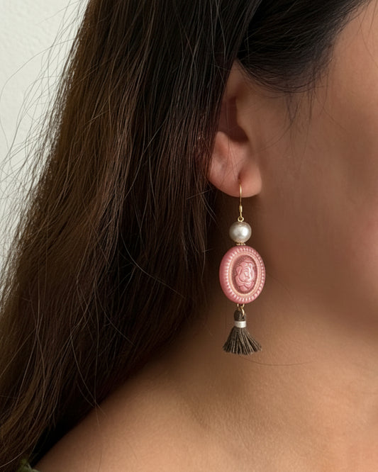 Close-up of a person wearing a pink tassel earring with a neutral background
